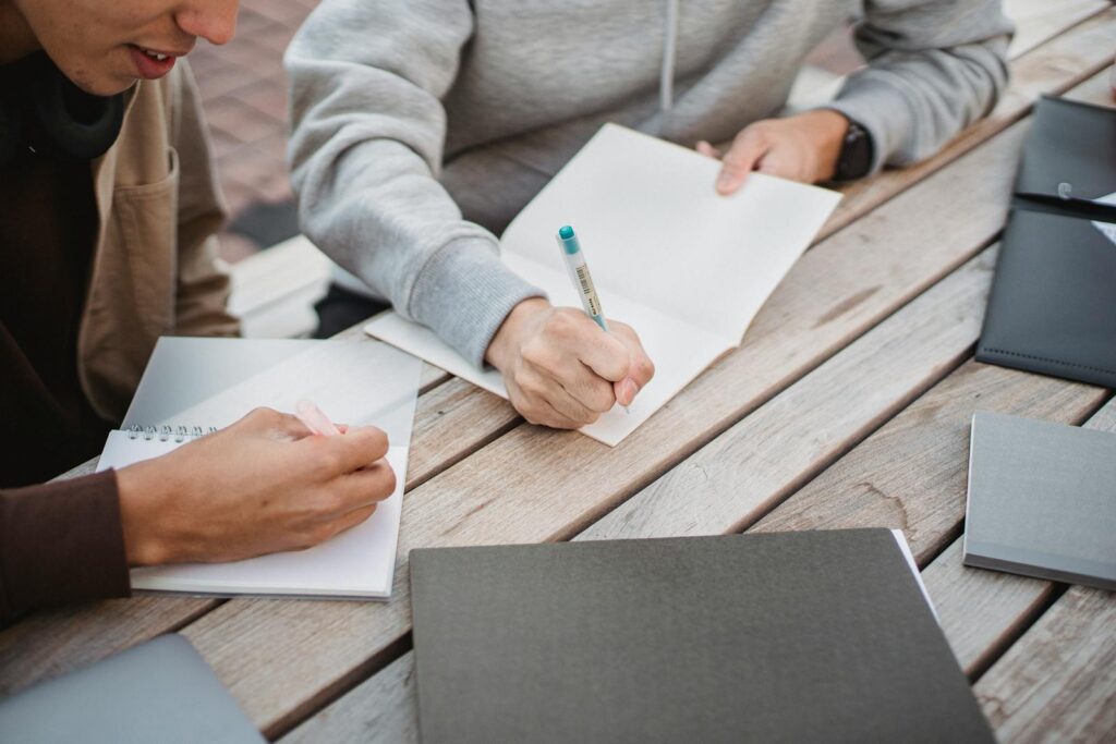 Die perfekte Hausarbeit schreiben: Tipps für Geschichte-Studierende 3 High angle crop male students in casual clothes taking notes in copybooks while working on home assignment together in park